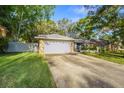 Quaint one-story home with stone detailing and a spacious driveway, surrounded by lush green grass and a light-colored fence at 14 Idlewilde Dr, Safety Harbor, FL 34695