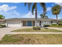 Inviting home featuring a well-manicured lawn, brick driveway, palm trees, and a bright blue double door at 3910 Doral Dr, Tampa, FL 33634