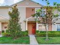 Inviting townhome facade with a vibrant red front door, manicured landscaping, and lush green lawn at 30340 Elderwood Dr, Wesley Chapel, FL 33543