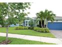 Charming one-story house featuring a manicured lawn, trimmed bushes, palm trees, and a blue garage door at 6417 Blue Sail Ln, Apollo Beach, FL 33572