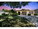 Charming single-story home with a three car garage and mature landscaping at dusk at 11383 Pickford St, Spring Hill, FL 34609