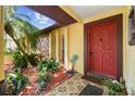 Inviting front porch with decorative red door, lush tropical plants, and stone accents at 11383 Pickford St, Spring Hill, FL 34609