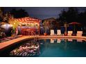 Backyard pool and outdoor lounge area with lighting, seating, and a tiki bar, perfect for evening enjoyment at 9201 86Th Ave, Seminole, FL 33777