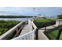 Dock with a wooden walkway leading to a boat lift on the water, framed by lush green bushes and a chain link fence at 3302 W Shell Point Rd, Ruskin, FL 33570