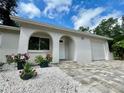 Stunning home with an arched entry, white stucco, a brick driveway, and vibrant landscaping, creating a warm welcome at 11241 Temple Ct, Seminole, FL 33772