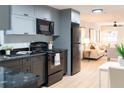 Well-lit kitchen with gray cabinetry, black appliances, light wood floors, and open to living room at 8303 N 17Th St, Tampa, FL 33604