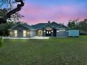 Inviting single-story home exterior with lush green lawn, dusk sky, and elegant stone-accented entry at 11268 Shivering Owl Ave, Weeki Wachee, FL 34614