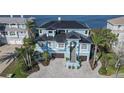 Aerial view of a light blue waterfront home with palm trees, a dark roof, and a driveway made of patterned pavers at 2111 Alexis Ct, Tarpon Springs, FL 34689