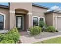 Home's welcoming entryway with arched doorway, manicured bushes, and a brick path at 14227 Alistar Manor Dr, Wimauma, FL 33598