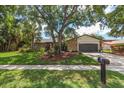 Charming single-story home with stone facade, a two-car garage, and a lush, landscaped front yard with mature oak tree at 50 Pine Lake Dr, Oldsmar, FL 34677