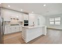 Modern kitchen with white cabinets, stainless steel appliances, a large island, and wood flooring at 11447 Shoreline Trl, Parrish, FL 34219