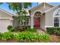 Inviting front exterior featuring a red door, mature landscaping, and a neutral exterior at 16522 Ivy Lake Dr, Odessa, FL 33556