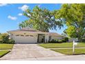 Inviting single-story home with a well-kept lawn, mature trees and a two car garage on a sunny day at 2961 Stockwood Dr, Clearwater, FL 33761