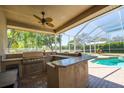 A screened in patio with an outdoor kitchen, bar and in-ground pool and view of the manicured backyard at 5807 Thoreau Pl, Lithia, FL 33547