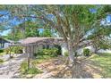 Single-story home featuring a covered driveway, lush landscaping and a large tree at 7703 W Hiawatha St, Tampa, FL 33615