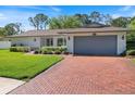 A single-story home with a brick driveway and two-car garage and mature landscaping at 2673 Clubhouse S Dr, Clearwater, FL 33761