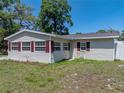 Exterior view featuring a house with light siding, red shutters, flower bed, and green lawn at 34477 Poinsettia Pl, Dade City, FL 33523