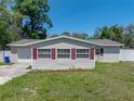 Charming home exterior features light siding, red shutters, green lawn, a garage, and a long driveway at 34477 Poinsettia Pl, Dade City, FL 33523