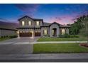 Charming two-story home with gray stucco, tile roof, stone accents, manicured lawn at dusk at 14421 Swiss Bridge Dr, Lithia, FL 33547