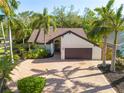 Charming home featuring a well-manicured lawn, mature palm trees, and a brick driveway leading to a two-car garage at 2966 Longbrooke Way, Clearwater, FL 33760