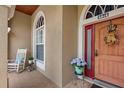 Inviting front porch featuring a cozy rocking chair, decorative flowers, and a wooden front door at 9916 Preakness Stakes Way, Dade City, FL 33525