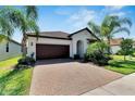 Beautiful one-story home with a well-maintained brick driveway, mature landscaping, and a brown tile roof on a sunny day at 16840 Whisper Elm St, Wimauma, FL 33598