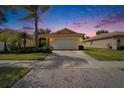 Lovely house featuring a brick driveway, 2-car garage, and palm trees set against a pink and purple sky at 16261 Amethyst Key Dr, Wimauma, FL 33598