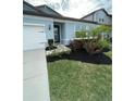 Landscaped front yard featuring a vibrant green lawn and a variety of plants and mulch surrounding the home's entrance at 6398 Bradford Woods Drive, Zephyrhills, FL 33542