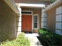 Inviting entrance with a bright orange double door, lush landscaping, and a covered porch area at 6130 Whimbrelwood Dr, Lithia, FL 33547
