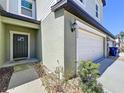 Close-up of a two-story townhome featuring a garage door, front door, lush landscaping, and neutral color palette at 32046 Powderpuff Mimosa Dr, San Antonio, FL 33576