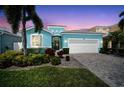 Beautifully landscaped home with a turquoise exterior, paved driveway, and lush tropical foliage at sunset at 424 Bahama Grande Blvd, Apollo Beach, FL 33572