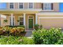 Inviting home featuring a covered front porch with well kept shrubs, a green door, and a two-car garage at 13312 Tiger Lilly Ln, Tampa, FL 33625
