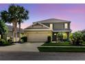 Charming two-story home featuring a well-manicured lawn, palm trees, and an attached two-car garage at dusk at 27094 Carolina Astor, Wesley Chapel, FL 33544