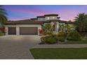 Elegant stucco home featuring a tile roof, three-car garage, paver driveway, and meticulously manicured landscaping at 949 Symphony Isles Blvd, Apollo Beach, FL 33572