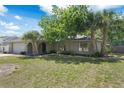 Charming single-story home featuring a two-car garage, arched entryway, and mature palm trees under a sunny sky at 5263 Kirkwood Ave, Spring Hill, FL 34608