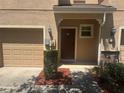 Welcoming townhouse entrance featuring a brown door, small shrubbery, and a tan colored garage door at 778 Spring Flowers Trl, Brandon, FL 33511