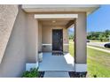 Covered front porch features a black front door, modern exterior lighting, and neutral stucco columns at 16894 Delia St, Wimauma, FL 33598