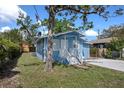 View of the light blue home with lush green lawn and mature trees at 8624 N Semmes St, Tampa, FL 33604