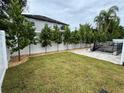 Large backyard with green lawn, white vinyl fence, trees and a pool covered with a net at 3910 W San Carlos St, Tampa, FL 33629