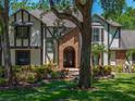 Charming Tudor-style home featuring a brick entrance, lush landscaping, and mature trees at 13004 Bell Creek Chase, Riverview, FL 33569