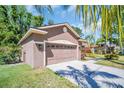 A two-car garage with a concrete driveway, exterior lighting, and well-maintained landscaping in the background at 1135 Wyndham Lakes Dr, Odessa, FL 33556