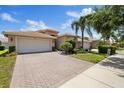 View of the home with a brick driveway, two-car garage, and palm tree in the front yard at 16055 Golden Lakes Dr, Wimauma, FL 33598