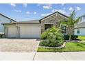 Beautiful single-story home featuring stone accents, a two-car garage, manicured landscaping, and a brick paved driveway at 21506 Snowy Orchid Ter, Land O Lakes, FL 34637