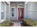 Close-up of a red front door with sidelights, enhanced by beautiful landscaping and lush greenery at 8463 Dunham Station Dr, Tampa, FL 33647
