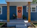 Close-up of a coral front door with a wreath, flanked by wooden pillars and plants at 10562 Lake Dr, Seminole, FL 33772