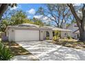 Single-story home with a well-manicured lawn, mature trees, and a large two car garage at 914 Woodland Dr, Palm Harbor, FL 34683