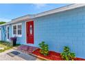 Bright blue home featuring a vibrant red front door, surrounded by lush landscaping and charming brick accents at 9206 Wood Lake Blvd, Tampa, FL 33615