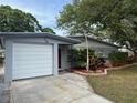 Single story home featuring an attached garage, red door, tropical landscaping and mature trees at 1542 Sherwood St, Clearwater, FL 33755