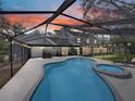 Backyard view of a screened-in pool and hot tub with string lights, surrounded by lush greenery and a colorful sunset at 17515 Drake Ct, Lutz, FL 33559