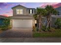 Charming two-story home features a two-car garage, brick driveway, and well-maintained landscaping at dusk at 31779 Asbury Ave, Wesley Chapel, FL 33545